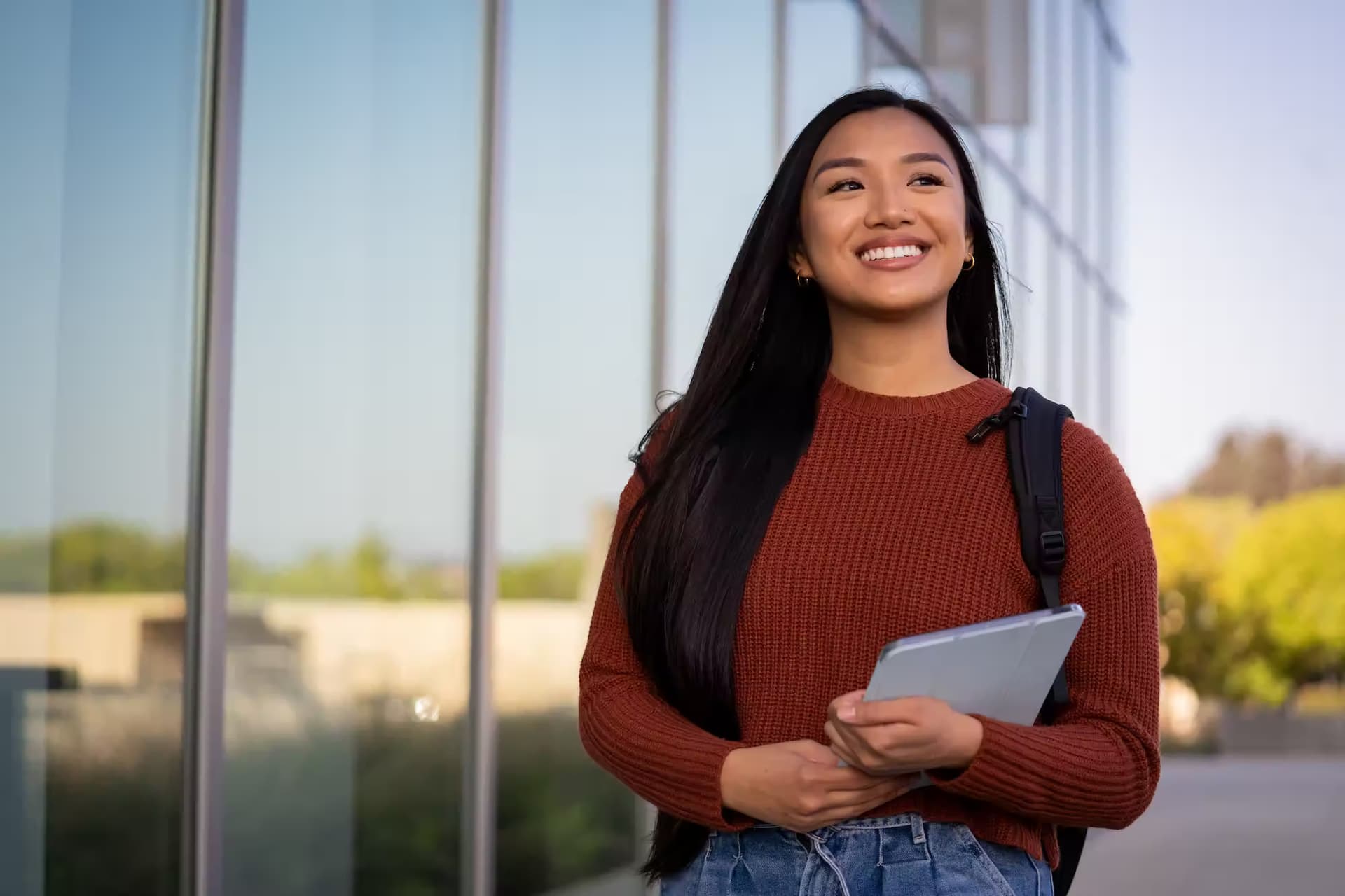 A female student walking outside with a tablet infront of a glass building